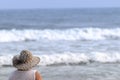 Unidentified woman with big beach hat looks at the ocean waves on the shore of Guaruja