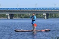 An unidentified young man holds a paddle while standing on a board in the middle of a wide river. Royalty Free Stock Photo