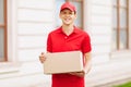 A uniformed courier holds an empty cardboard box in the open air. Delivery service