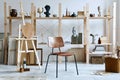 Unique artist workspace interior with stylish teak commode, wooden easel, bookcase, artworks, painting accessories, decoration.