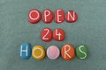 Open 24 Hours, commercial slogan or sign composed with handmade multi colored stone letters over green sand