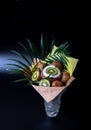 Unique festive bouquet of coconut, kiwi and palm twigs on a black background. Fruit bouquet. Fruits and Vegetables of the Healthy