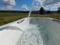 Unique photo of a water stream running into white bath tub on a green grass field landscape with Pine trees under blue cloudy sky Royalty Free Stock Photo