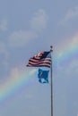 United States and Oklahoma flags flying high in front of rainbow sky with a few clouds