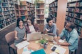 Unity and connection of people. Four multi ethnic students friends, doing research in library together, wearing casual clothes, e