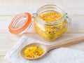 Universal seasoning in an open clip top glass jar and wooden spoon on a white wooden table. Seasoning contains salt and dried