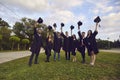 University graduate students raising mortarboards up outdoors. College grads in gowns celebrating commencement day Royalty Free Stock Photo