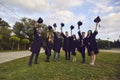 University graduate students raising mortarboards up outdoors. College grads in gowns celebrating commencement day