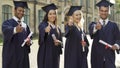 University graduates in academic regalia holding diplomas, putting thumbs-up