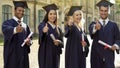 University graduates in academic regalia holding diplomas, showing thumbs-up