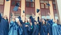 University graduates  throwing graduation hats in the air. Group of happy graduates in academic dresses near university building Royalty Free Stock Photo