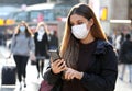 University student commuter walking using mobile phone wearing face mask protection as prevention for coronavirus in city airport