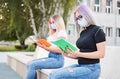 University student girls sitting and preparing for an exam - studying from booklets and wearing face mask to protect themselves