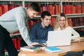 University students sitting together at table with books and laptop. Happy young people doing group study in library Royalty Free Stock Photo