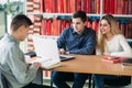 University students sitting together at table with books and laptop. Happy young people doing group study in library Royalty Free Stock Photo