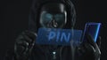 Hacker wearing black mask pulls PIN tab from a smartphone. Hacking concept