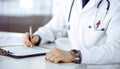 Unknown male doctor sitting and working with clipboard of medication history record in clinic at his working place