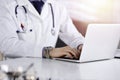 Unknown male doctor sitting and working with laptop in a darkened clinic, glare of light on the background, close-upof