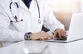 Unknown male doctor sitting and working with laptop in a darkened clinic, glare of light on the background, close-upof