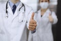 Unknown man-doctor and woman standing straight as a team and showing Ok sign with thumbs up in modern clinic. Medicine Royalty Free Stock Photo