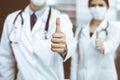 Unknown man-doctor and woman standing straight as a team and showing Ok sign with thumbs up in modern clinic. Medicine Royalty Free Stock Photo