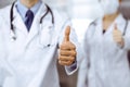 Unknown man-doctor and woman standing straight as a team and showing Ok sign with thumbs up in modern clinic. Medicine Royalty Free Stock Photo