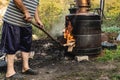Unknown man putting woods on fire on cooking Homemade illegal distillery on the farm making domestic brandy vodka Rakija whiskey