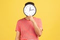 Unknown man in striped t-shirt hiding face behind big wall clock display, wasting his time, procrastination, bad organization of Royalty Free Stock Photo