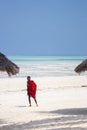 Unknown Masai man in red dress on beach with umbrella. African people concept. Maasai warrior on low tide background.