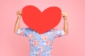 Unknown person hiding behind large red paper heart, holding symbol of love affection fondness