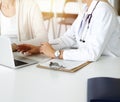 Unknown woman-doctor communicating with female patient in sunny clinic. Physician checks medical history record and exam Royalty Free Stock Photo