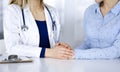 Unknown woman-doctor is holding her patient`s hands to reassure a patient, while sitting together at the desk in the