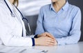 Unknown woman-doctor is holding her patient`s hands to reassure a patient, while sitting together at the desk in the