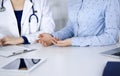 Unknown woman- doctor is listening to her patient, while sitting together at the desk in the cabinet in a clinic. Female Royalty Free Stock Photo