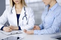 Unknown woman- doctor is listening to her patient, while sitting together at the desk in the cabinet in a clinic. Female Royalty Free Stock Photo