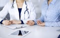 Unknown woman- doctor is listening to her patient, while sitting together at the desk in the cabinet in a clinic. Female Royalty Free Stock Photo