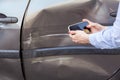 Unknown woman with mobile phone in hands taking picture of damaged part of car, photographing scratches and dents on auto door,