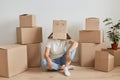 Unknown woman wearing white T-shirt sitting on the floor near cardboard boxes, posing with carton box on her head with drawing Royalty Free Stock Photo