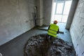 Unknown worker in protective clothes and orange safety helmet is making a cement floor screed in a flat of a high-rise