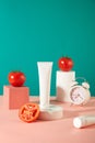 An unlabeled cosmetic tube is displayed on a white podium. Two tomatoes are placed on cubes next to an alarm clock. Turquoise and Royalty Free Stock Photo