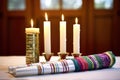 unlit shabbat candles with a torah and prayer shawl in the background