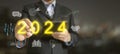 Unlock Success in 2024. A businessman points to the Glowing Text of 2024, surrounded by relevant Business Icons