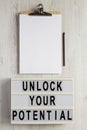 `Unlock your potential` on a lightbox, clipboard with blank sheet of paper on a white wooden surface, top view. Flat lay, overhe Royalty Free Stock Photo