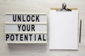 `Unlock your potential` on a lightbox, clipboard with blank sheet of paper on a white wooden surface, top view. Flat lay, overhe Royalty Free Stock Photo