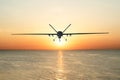 Unmanned military drone patrols the territory at sunset, flying above water surface. The view is straight ahead.