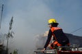 Unmarried Woman Fire Fighter With Protective Hat sitting on top of fire truck in the area of burning house