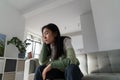 Unmotivated pensive Asian girl student age sits on couch in apartment leaning head on hand