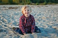 unny smiling laughing white Caucasian child kid blond boy, sitting playing with sand on beach at sunset