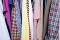 Unorganized clothes of different colors hanging in a wardrobe in mess close up, storage and order at home, cleaning and cluttering