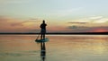 An unorthodox Jewish woman floats on a sappboard in the evening in golden reflections from the sunset on the sky and water